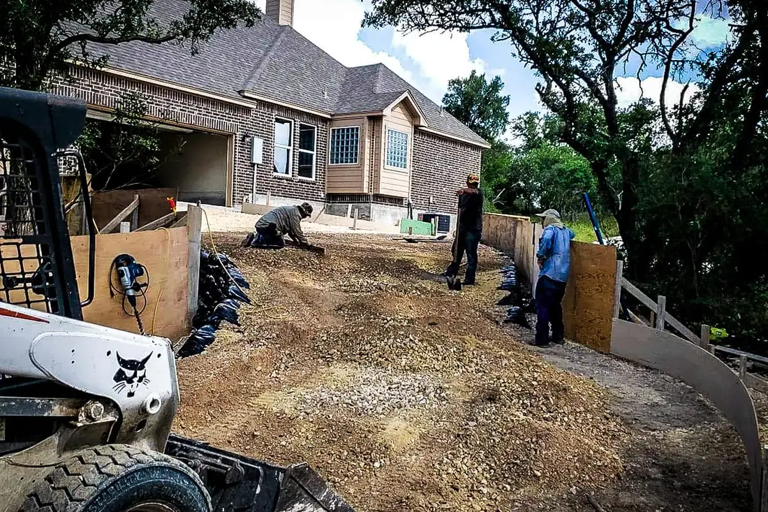 Crew spreading and levelling base rock for a concrete driveway in San Antonio