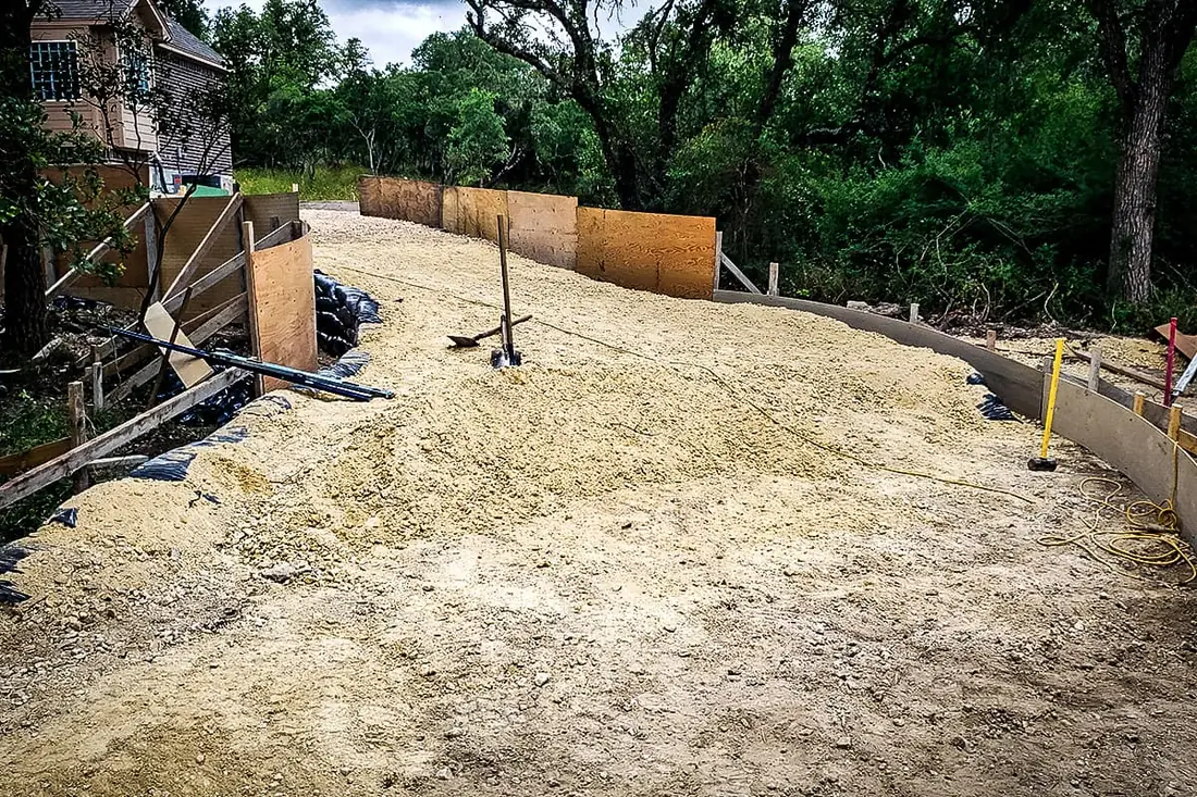 Graded base ready for a concrete driveway pour on a wooded lot near San Antonio
