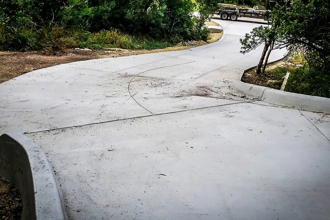 Curbed concrete driveway curving through Hill Country trees near San Antonio