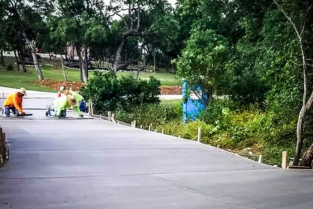 Crew finishing a long concrete driveway on a wooded Hill Country lot