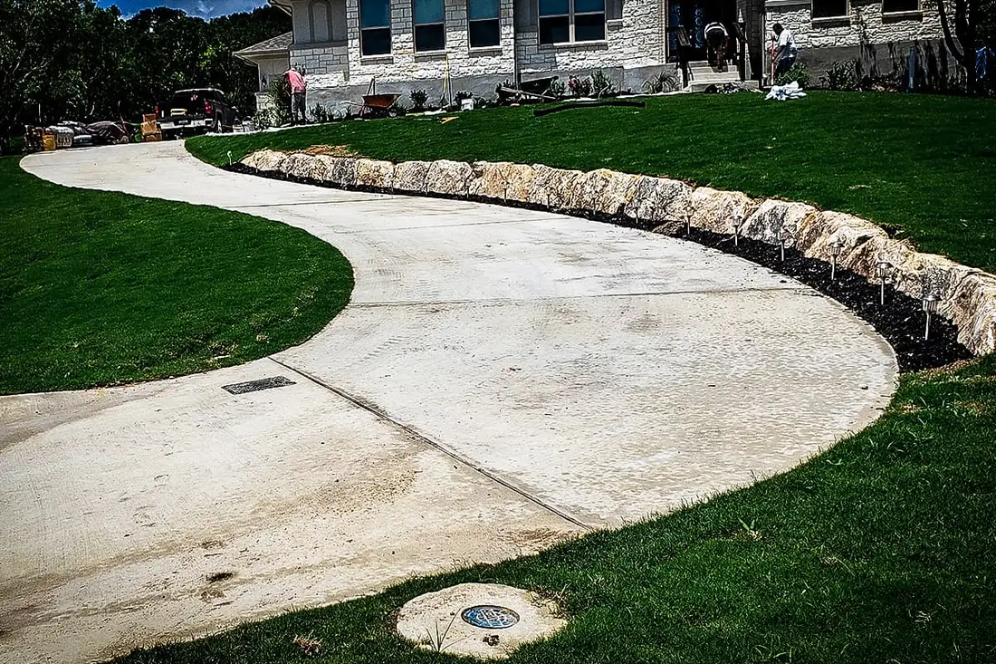 Concrete driveway edged with a limestone boulder border in San Antonio