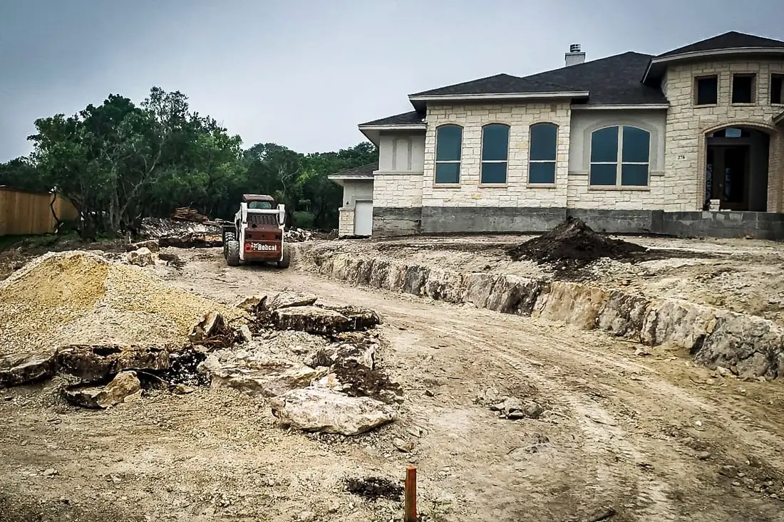 Skid steer cutting a driveway line through limestone at a San Antonio build