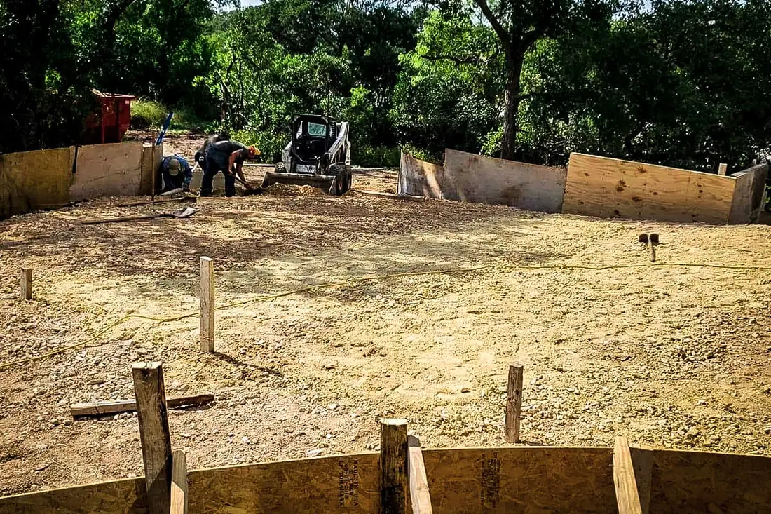 Crew grading a building pad with a skid steer before a concrete slab pour